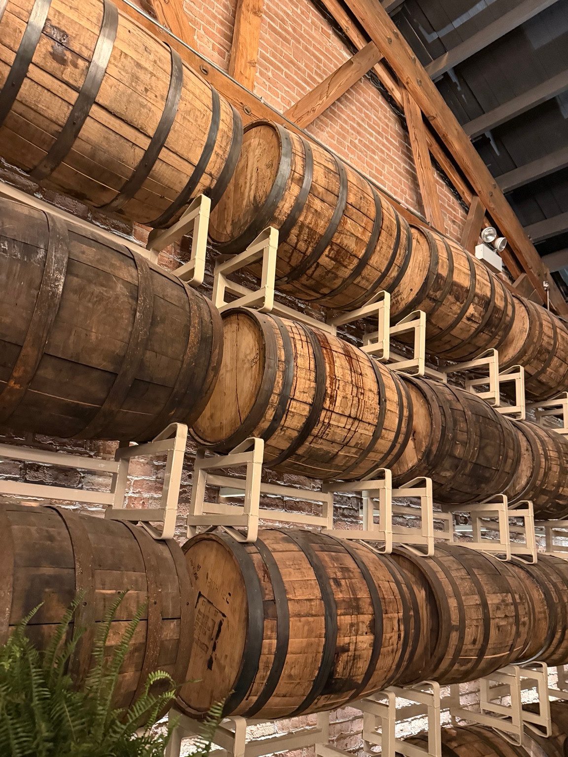 Close view of wooden barrels resting in pale metal racks against exposed brick at Goose Island Barrel House.