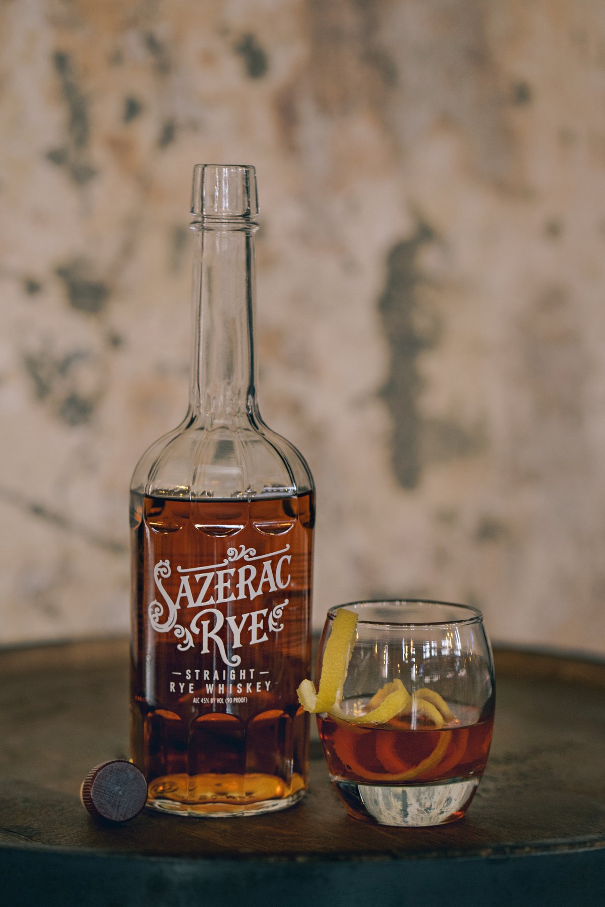 Sazerac Rye bottle beside a cocktail with lemon peel